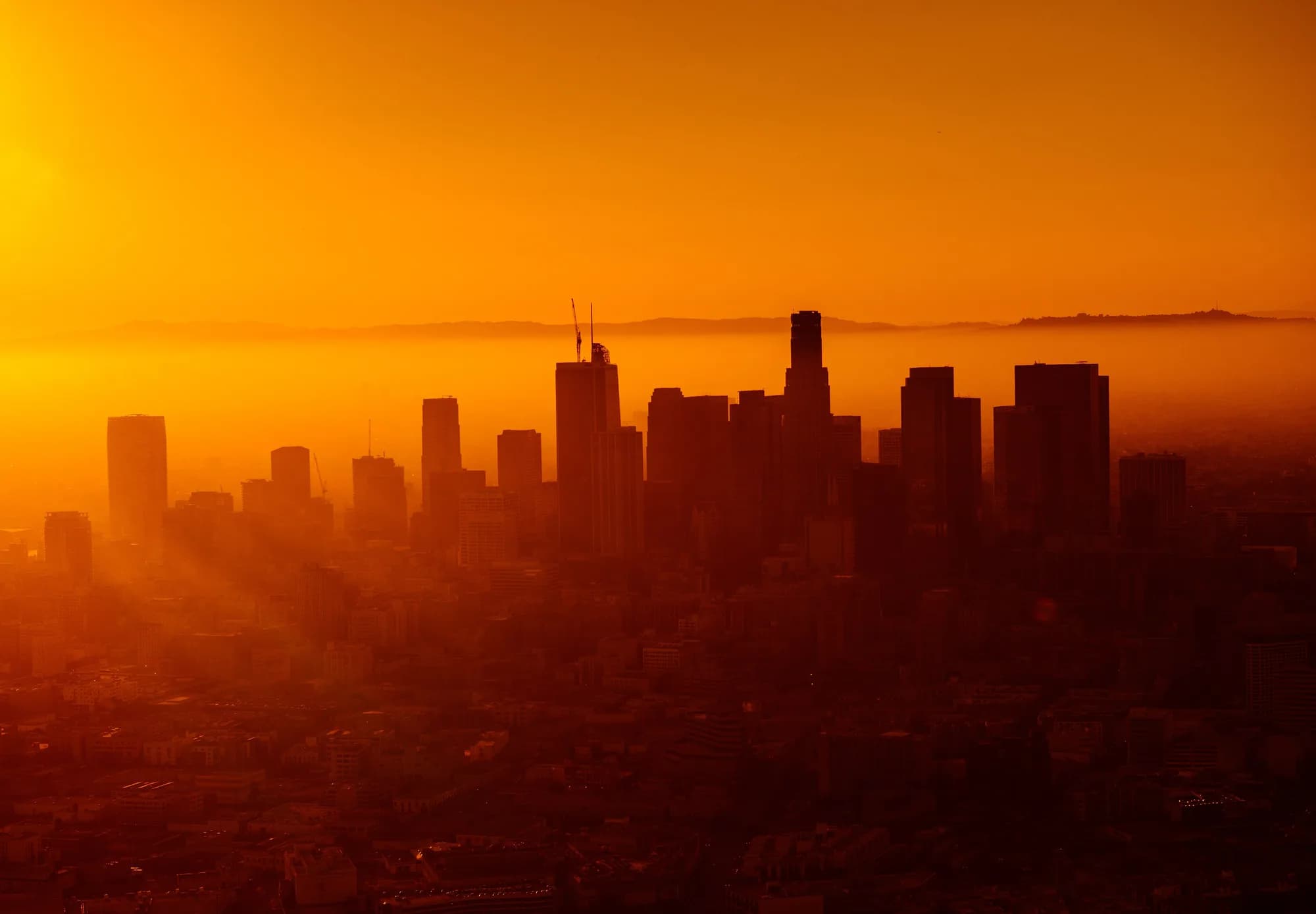 Downtown Los Angeles skyscrapers silhouetted in dense orange haze at sunset
