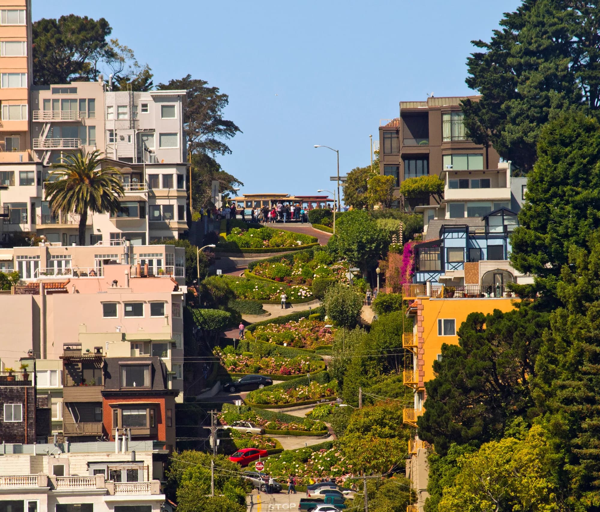 Lombard Street's brick switchbacks winding between houses and hedges, with a cable car waiting at the crest
